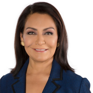 Headshot of woman with blue blazer and dark hair with gold earrings