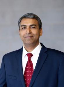 Photograph of Andre Ellis wearing a navy blue coat, white shirt and red tie