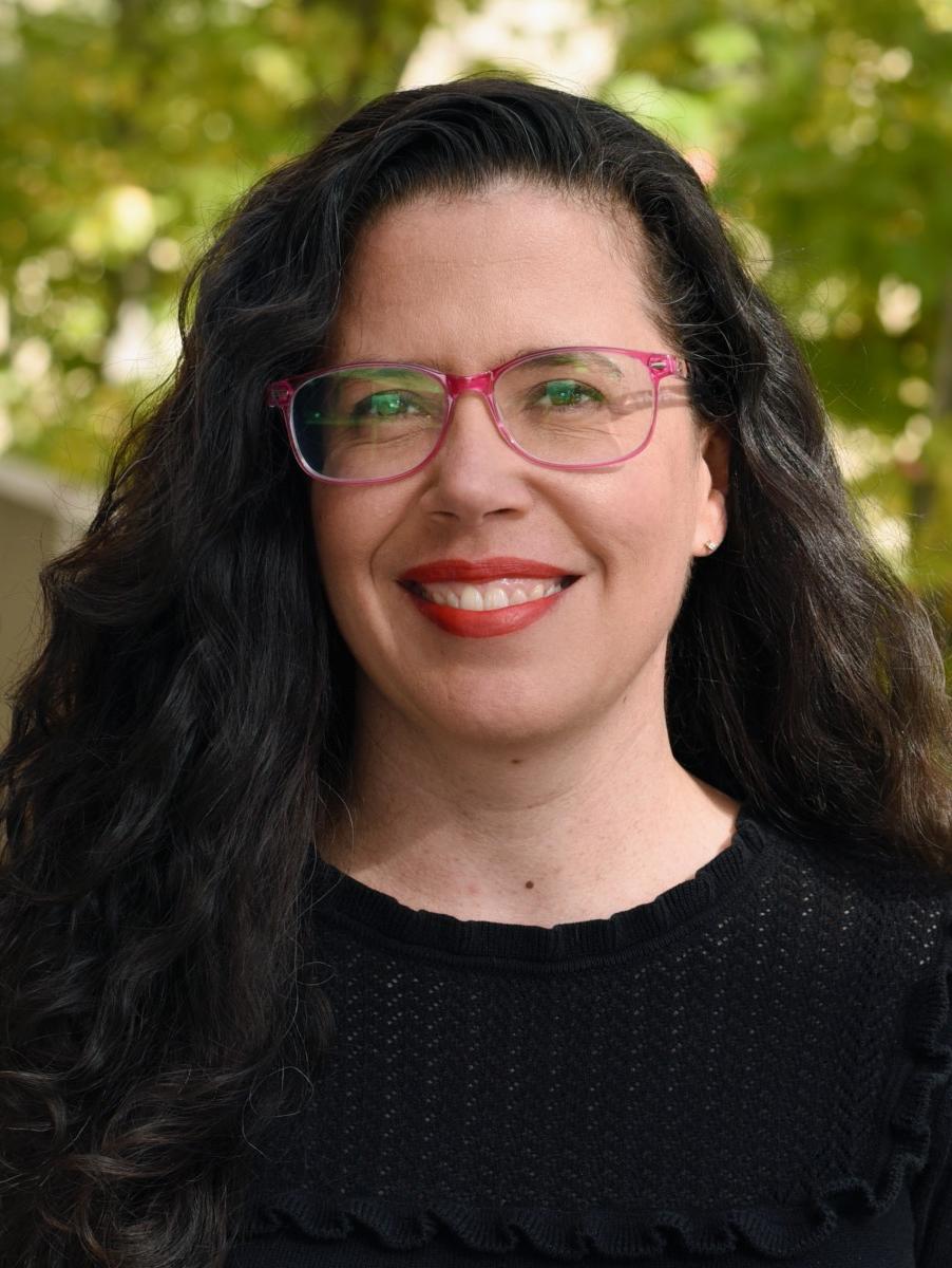 A person with long hair and glasses smiling.