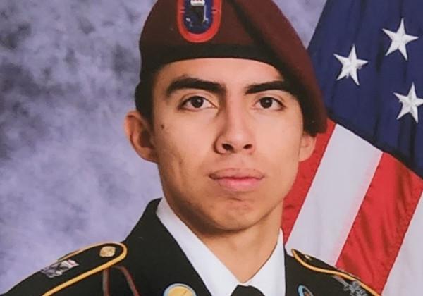 A person in a military uniform in front of an American flag.