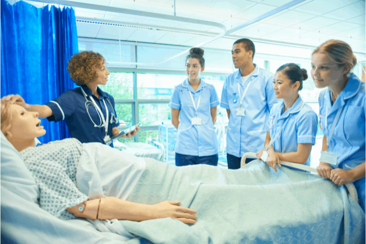 Instructor with nursing students at bedside in hospital.