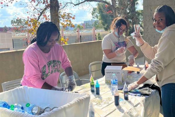 Three students smiling and creating a tie-dye shirt.