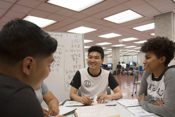 Group of students gathered in the library around a dry-erase board, studying. 