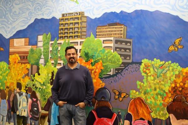 MA Student, Reynaldo Mora posing in front of a mural he painted 