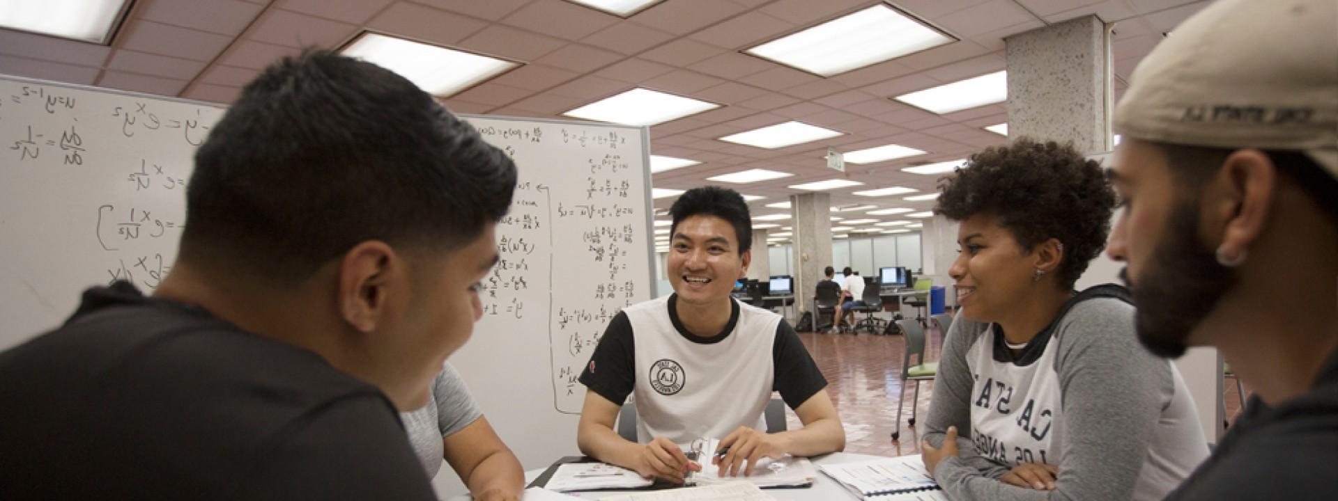 Group of students gathered in the library around a dry-erase board, studying. 